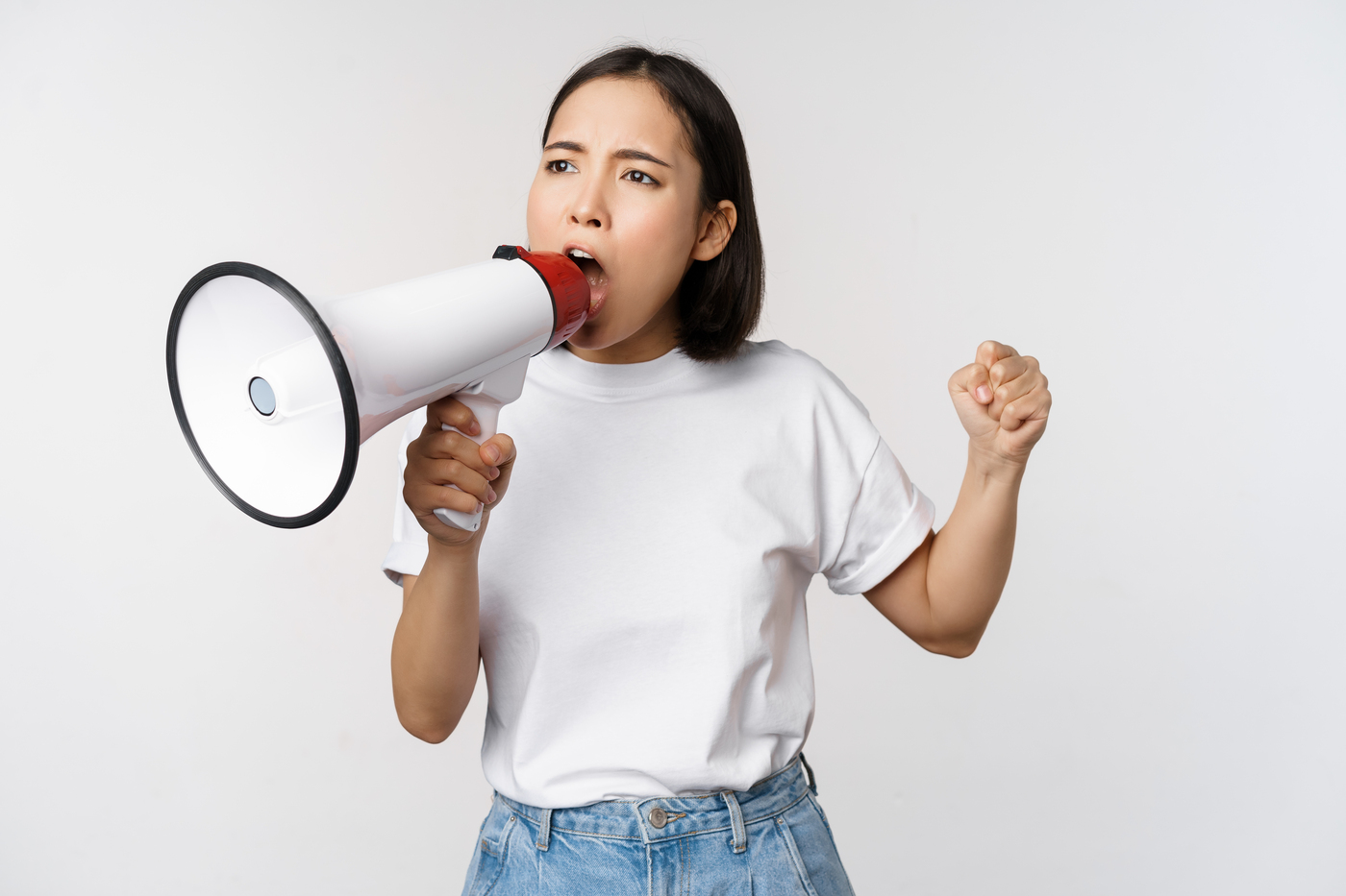 Asian girl shouting at megaphone, young activist protesting, using loud speakerphone, standing over white background
